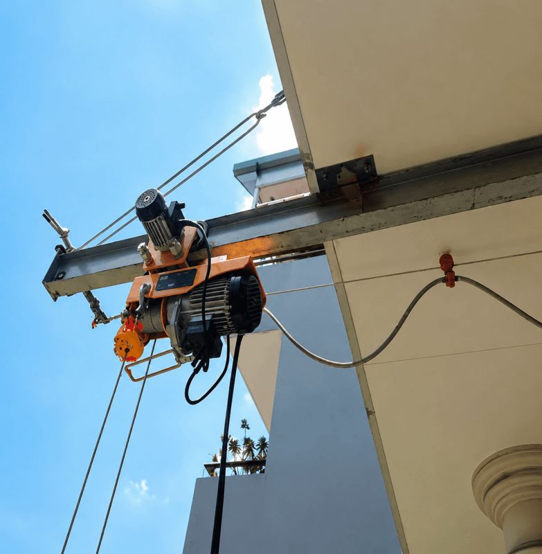 Tời điện mini màu cam gắn trên thanh ray ngoài mặt tiền tòa nhà