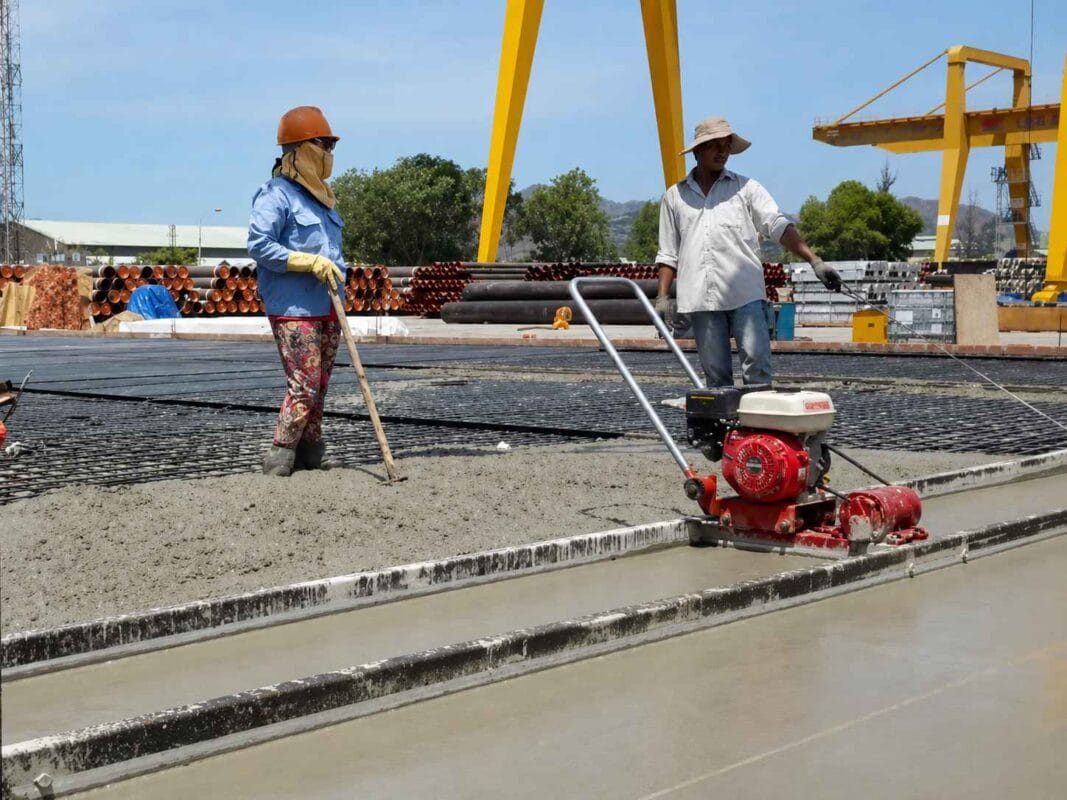 Cách chọn máy đầm bê tông đúng loại: dùi, bàn hay cóc? 4 Hai công nhân đang san phẳng và hoàn thiện mặt sàn bê tông tại công trường xây dựng. Cách chọn máy đầm bê tông đúng loại