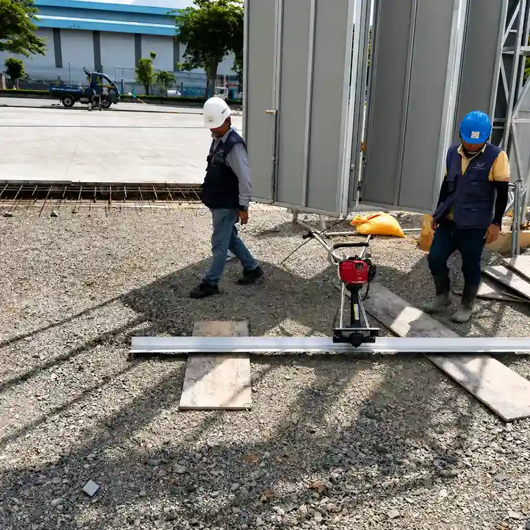 Hai công nhân đội mũ bảo hộ đang làm việc với máy san phẳng nền tại công trình xây dựng
